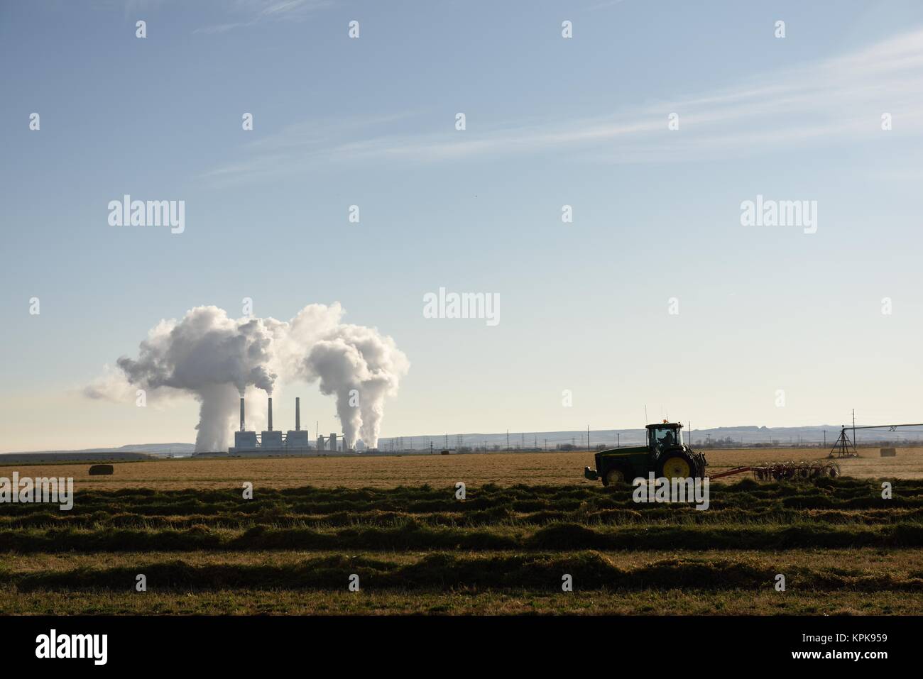 L'augmentation des émissions à partir de centrales au charbon gare cheminées avec un tracteur laboure un champ dans l'avant-plan, près de Wheatland, dans le Wyoming. Banque D'Images