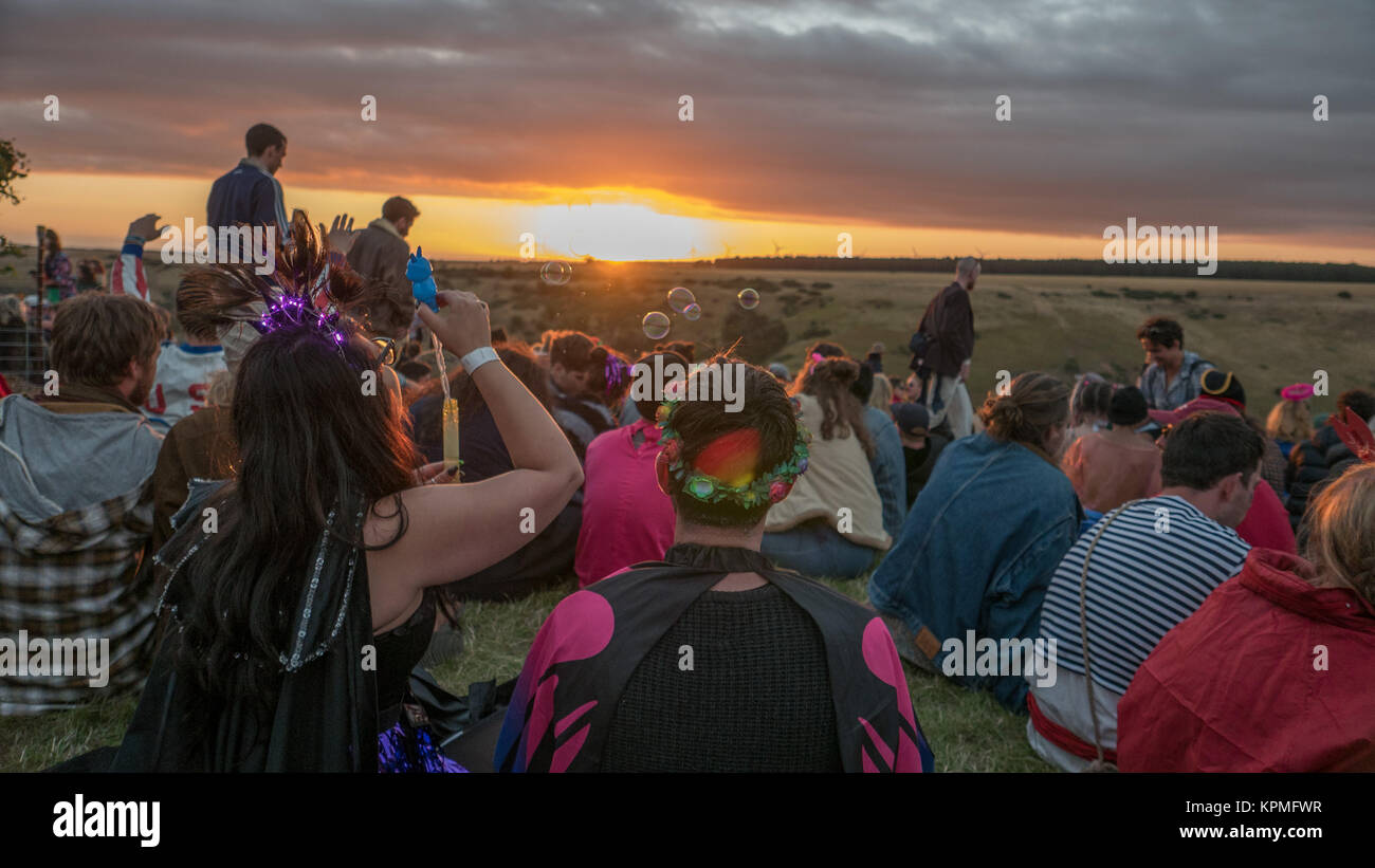 Les femmes assises dans la foule des spectateurs du festival de musique, regarder le coucher du soleil d'or tout en soufflant des bulles de savon. Banque D'Images