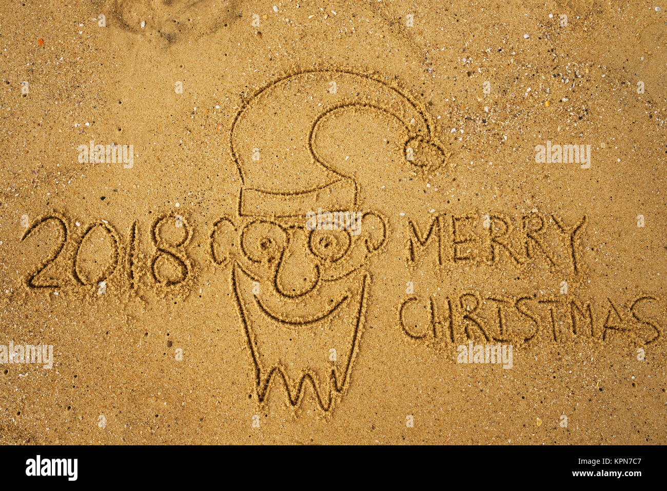 Joyeux Noël 2018 mots de l'écriture sur le sable de plage et drôle de visage de Père Noël. Banque D'Images