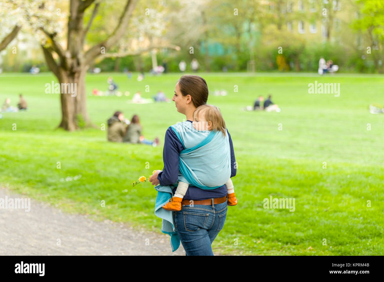 Une jeune mère portant son petit bébé dans une écharpe sur le dos et marcha dans beau temps ensoleillé par un parc. Les deux de rire et s'amuser Banque D'Images