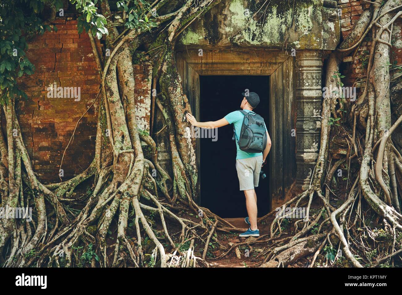 Jeune homme avec sac à dos venant d'anciens monuments sous les racines de l'arbre géant près de Siem Reap (Angkor Wat) au Cambodge Banque D'Images