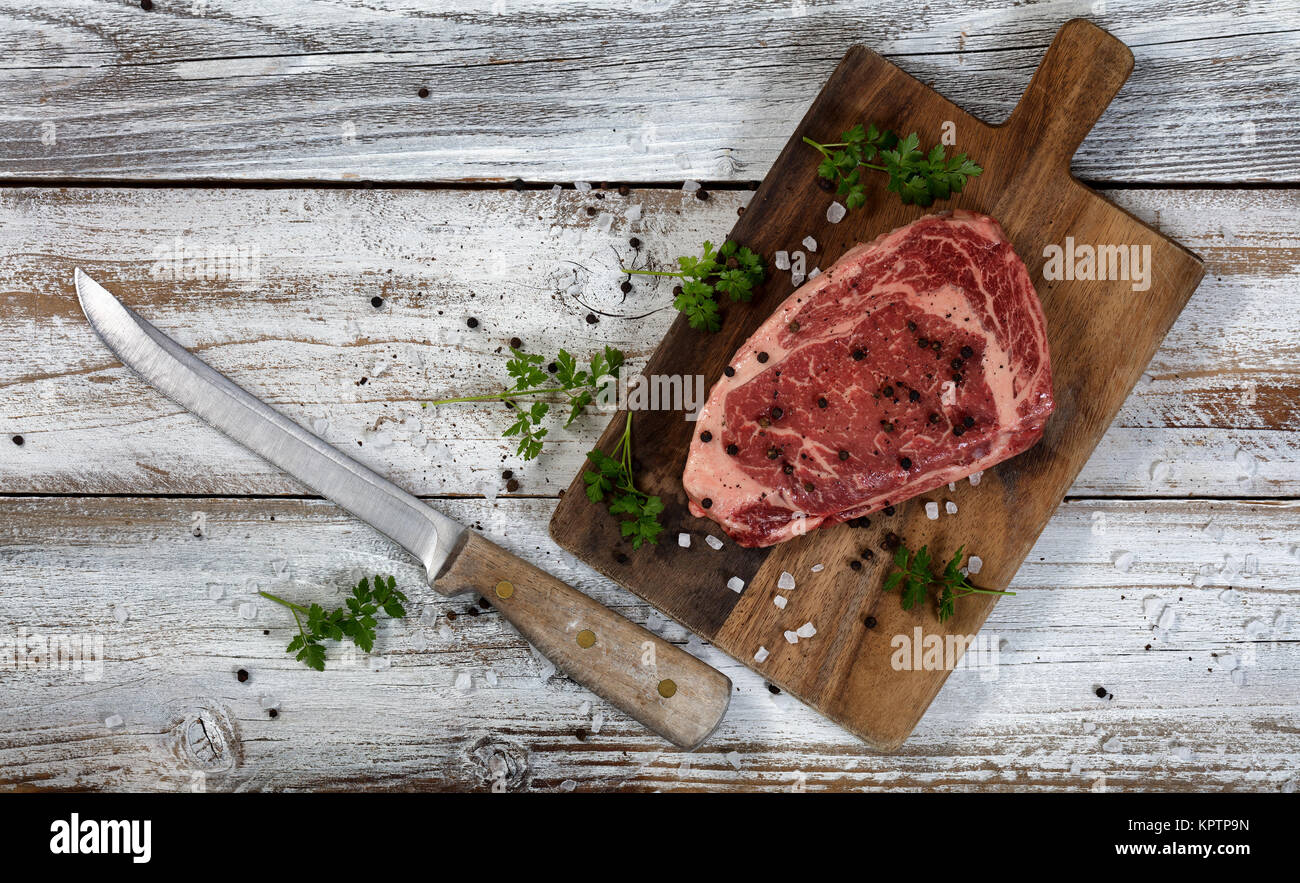 Tranche d'un steak cru avec grand couteau sur serveur en bois Banque D'Images