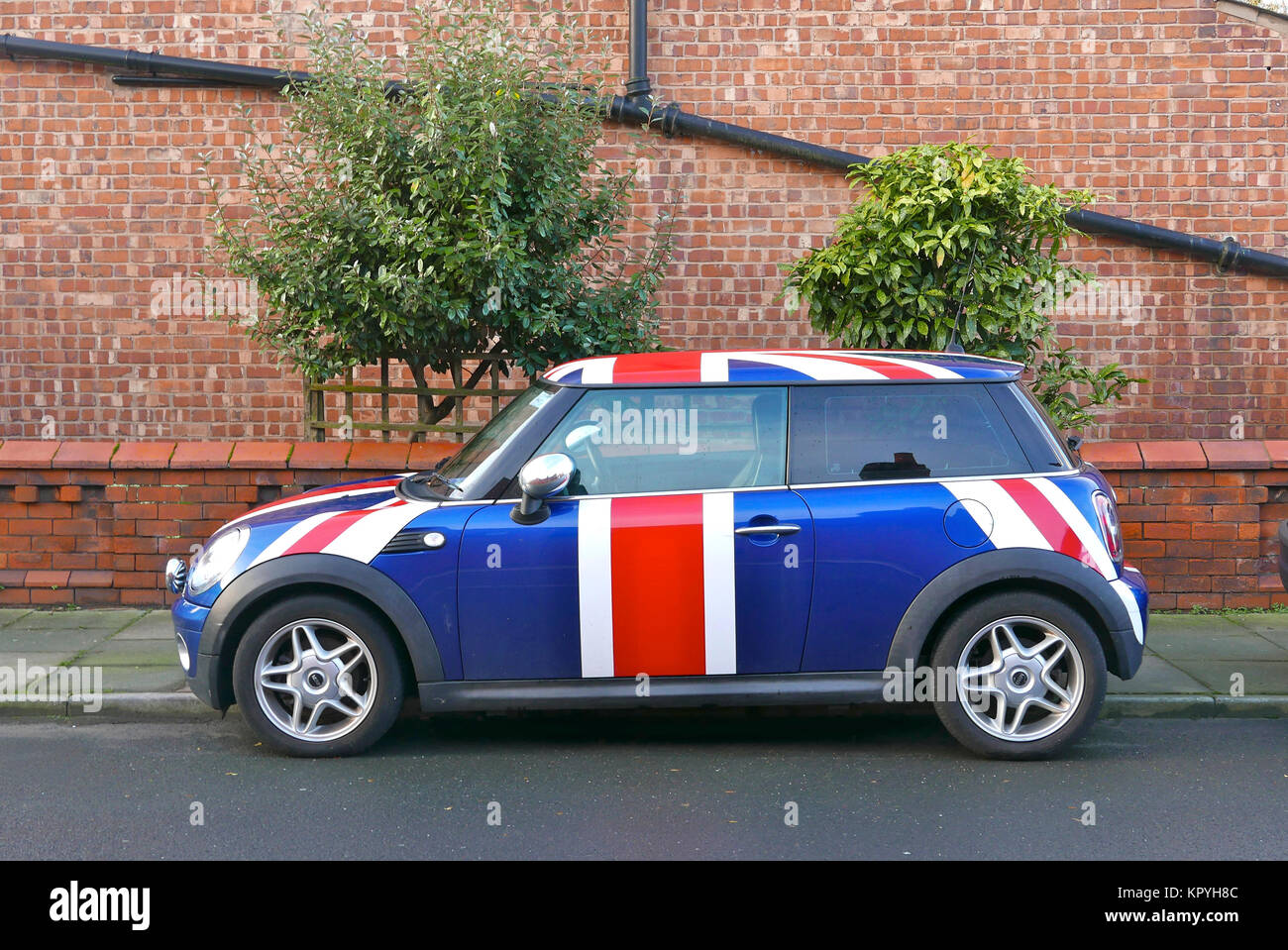 En voiture Mini Union jack livery stationné sur une route en face de deux arbres et mur de brique rouge Banque D'Images