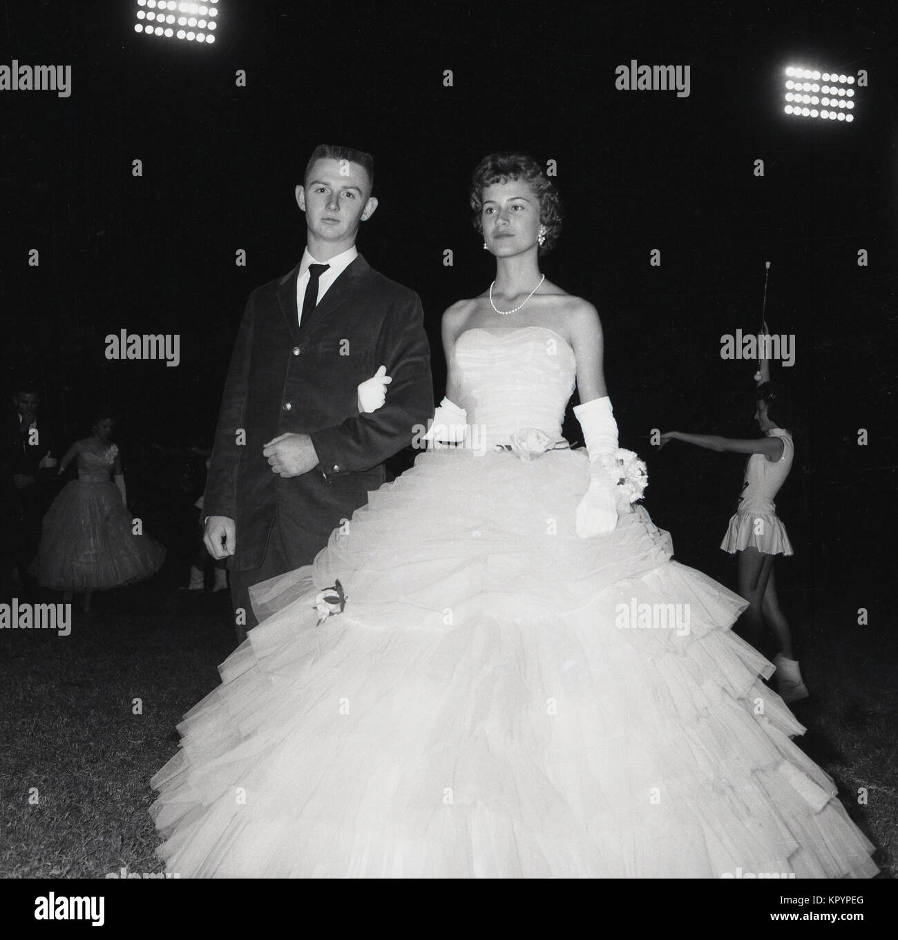 Années 1960, historique, du temps le soir, des projecteurs et défilé... un  jeune homme en cravate noire accompagne une jeune femme portant une robe de  bal magnifique collier et à l'extérieur à