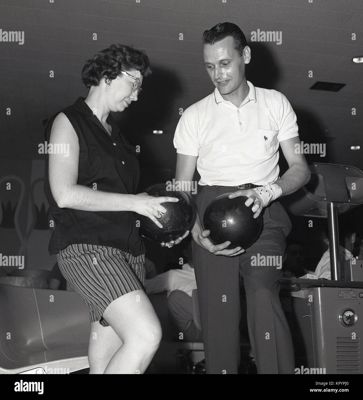 Années 1960, historiques, l'homme montrant une dame la manière correcte doigts doivent être placés dans les emplacements d'une boule de bowling à dix quilles alley, USA. Banque D'Images