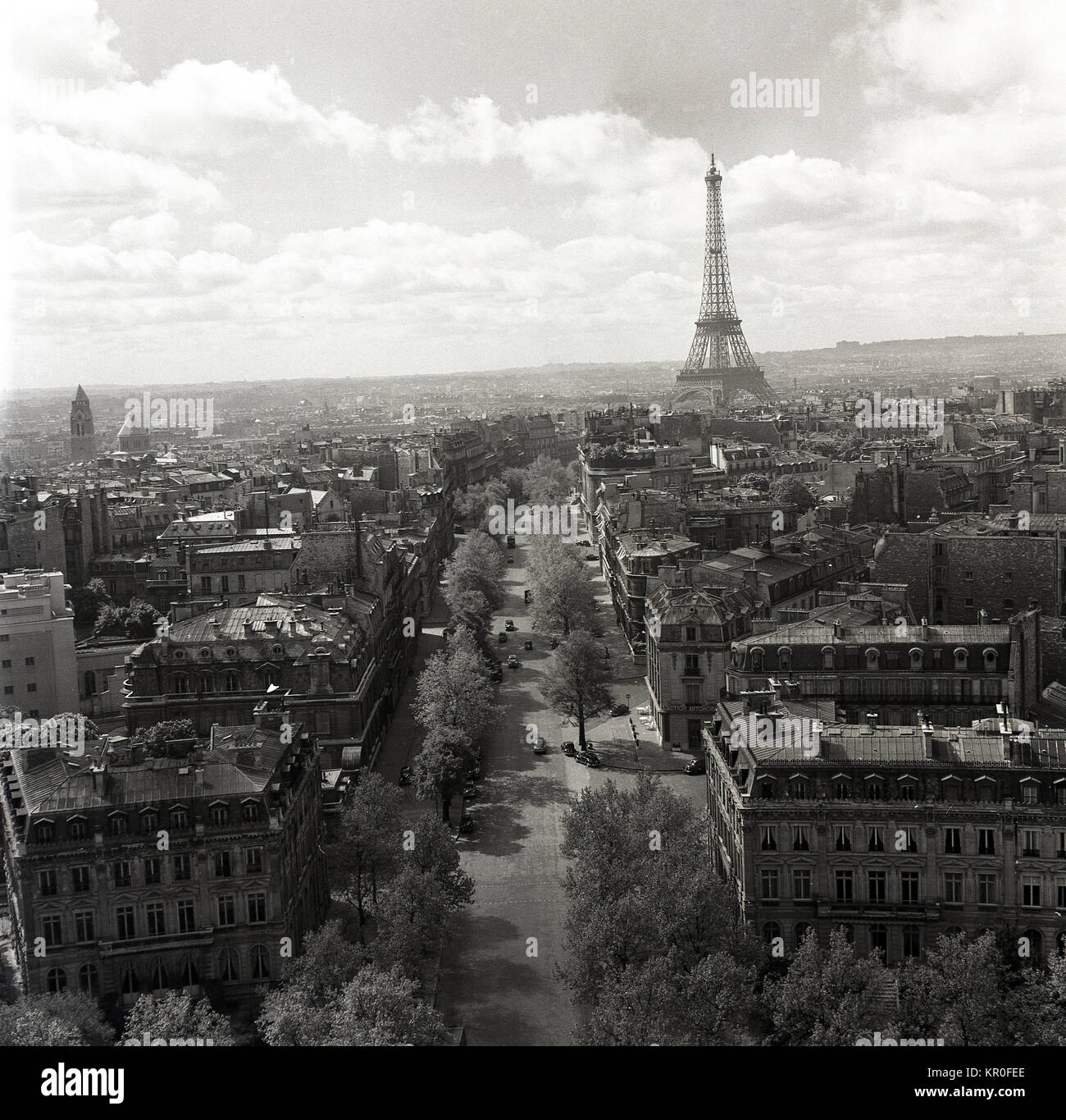 Années 1950, Paris, France, et un historique du passage d'un boulevard bordé d'arbres avec la célèbre tour en fer forgé, de la Tour Eiffel au loin. On peut voir en ce moment quelle est la taille et la définition de la tour a été comparée aux autres édifices de la ville qui ont une hauteur uniforme. Banque D'Images