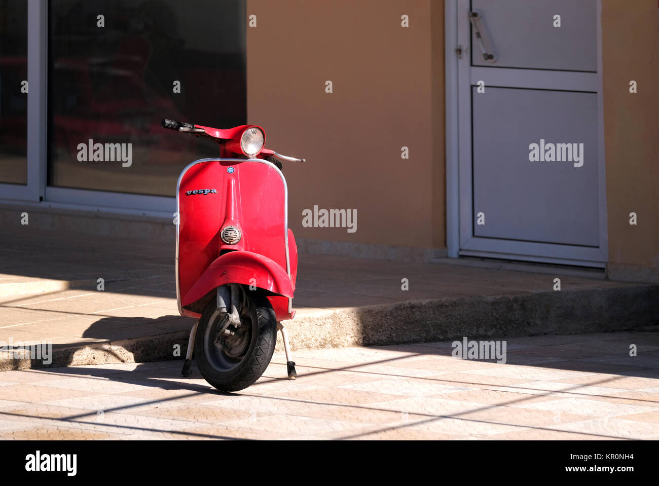 Un vieux scooter Vespa rouge garée sur un stand dans la rue. Malgré son âge, le scooter est en bon état et le soleil montre sa peinture rouge Banque D'Images