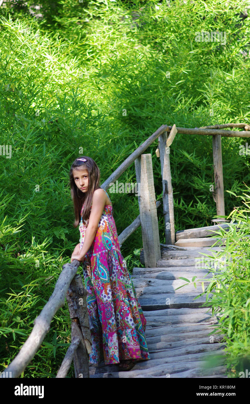 Jolie jeune fille debout sur un pont en bois dans le jardin vert. Banque D'Images