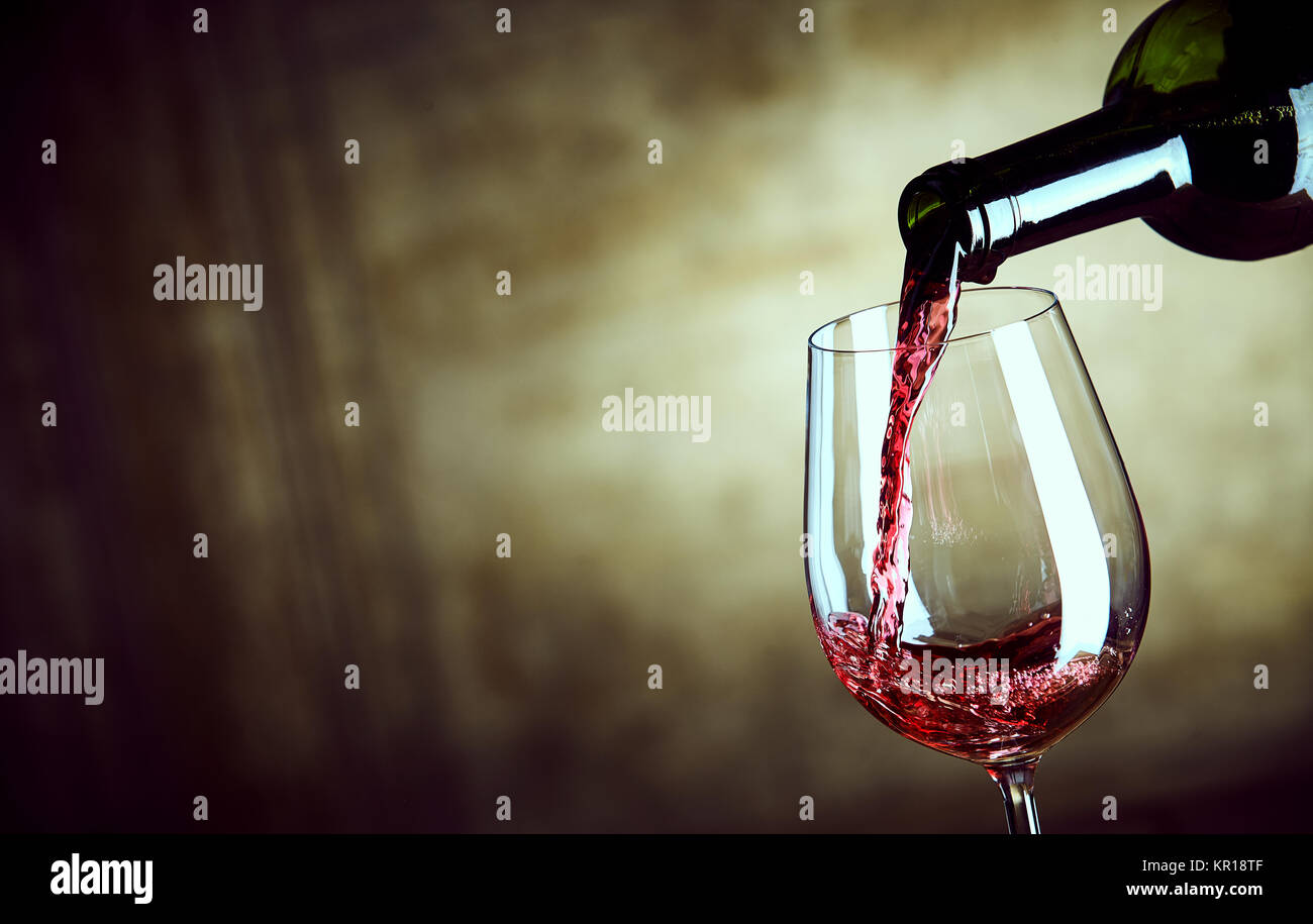 Servant un seul verre de vin rouge d'une bouteille avec une vue de près du col de la bouteille et le verre sur un fond brun résumé grand angle with copy space Banque D'Images