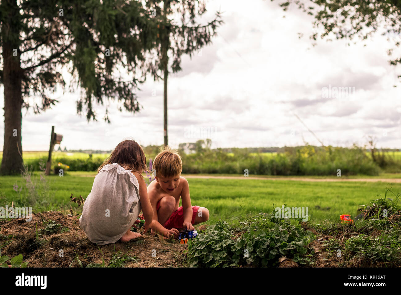 Garçon et fille jouant avec les petites voitures dans le jardin Banque D'Images