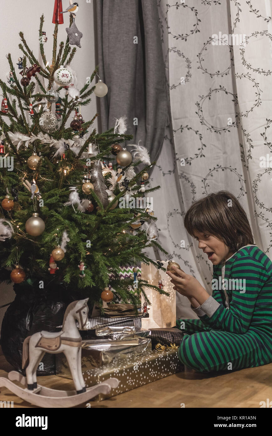 Garçon assis par l'arbre de Noël wearing pajamas Banque D'Images