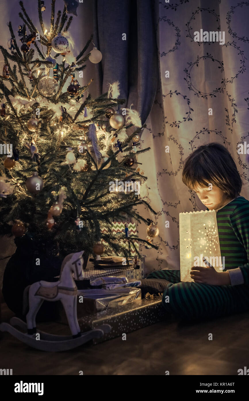 Garçon assis à côté d'un arbre de Noël à la lumière à un Banque D'Images