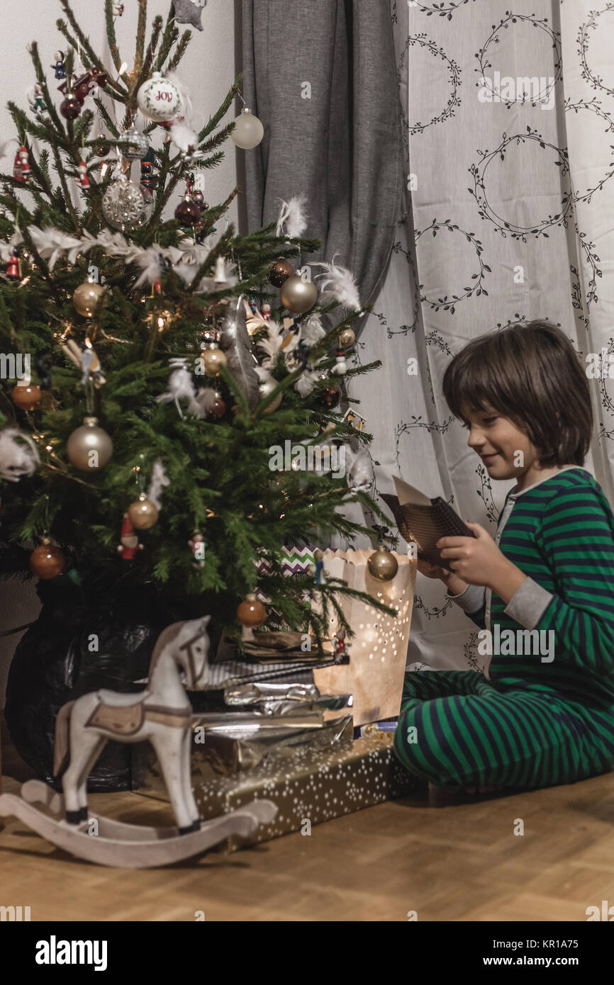 Garçon en pyjama à la recherche de cadeaux sous un arbre de Noël Banque D'Images