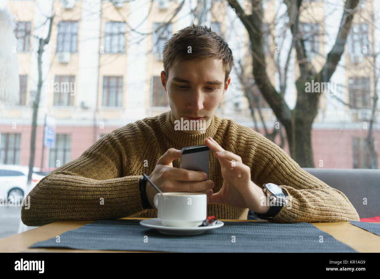 Homme assis dans le café shop reading text message on mobile phone Banque D'Images