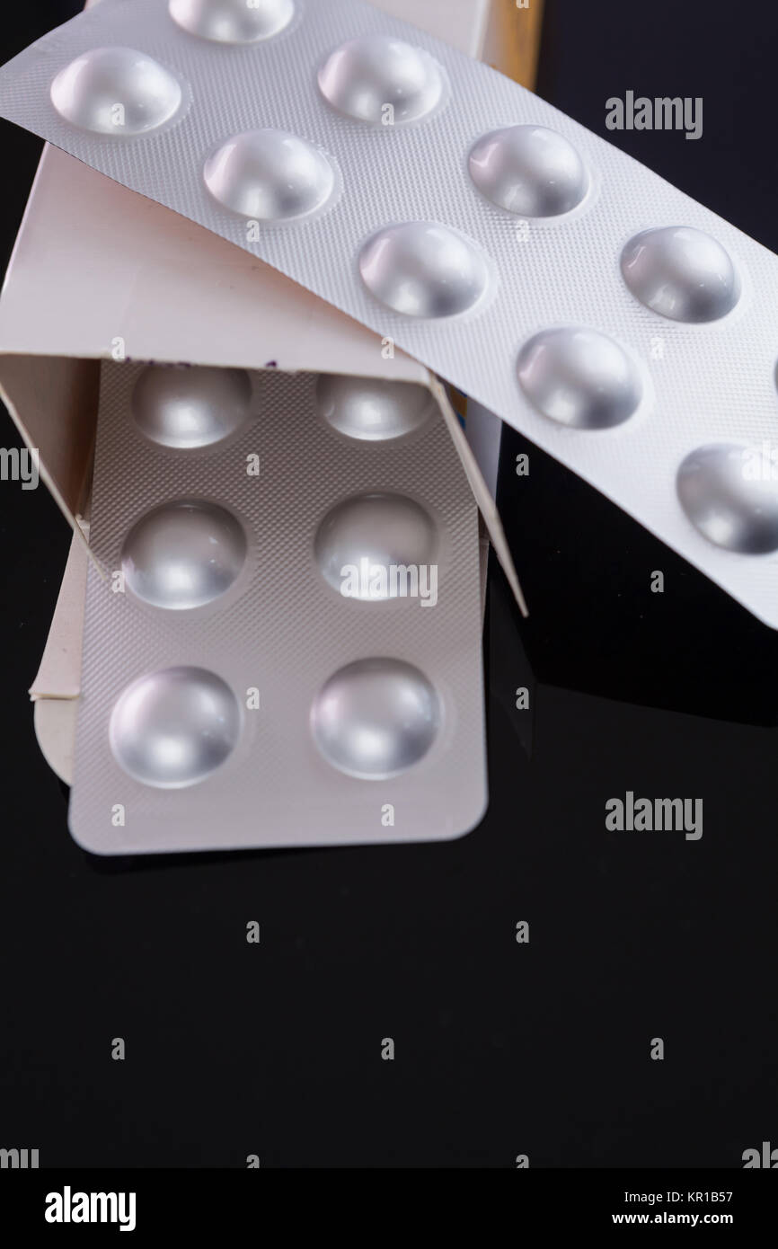 Silberne Blisterpackung von kleinen Pillen zusammen mit Schachtel mit zusätzlichen Packungen durch den offenen Deckel über einem schwarzen Hintergrund dans un Gesundheits-Konzept Banque D'Images