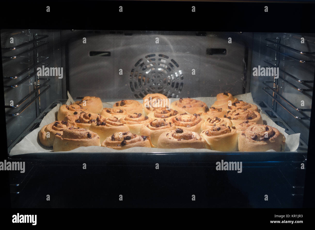 Noël sucré fait maison de levure à la cannelle et aux raisins avec canneberge, sur du papier sulfurisé sur la plaque de cuisson, à l'intérieur d'un four. Banque D'Images