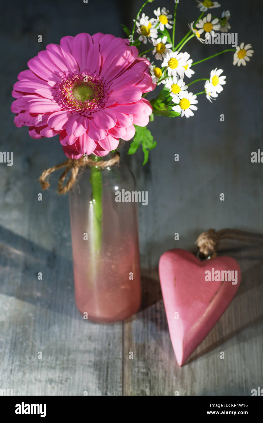 Still Life with gerbera rose et un coeur dans un vase en verre sur une table en bois Banque D'Images