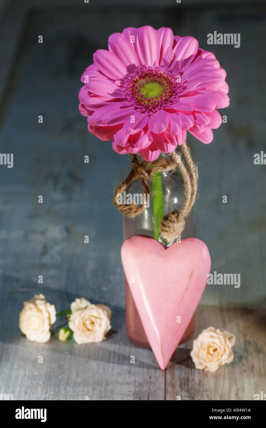 Still Life with gerbera rose et un coeur dans un vase en verre sur une table en bois Banque D'Images