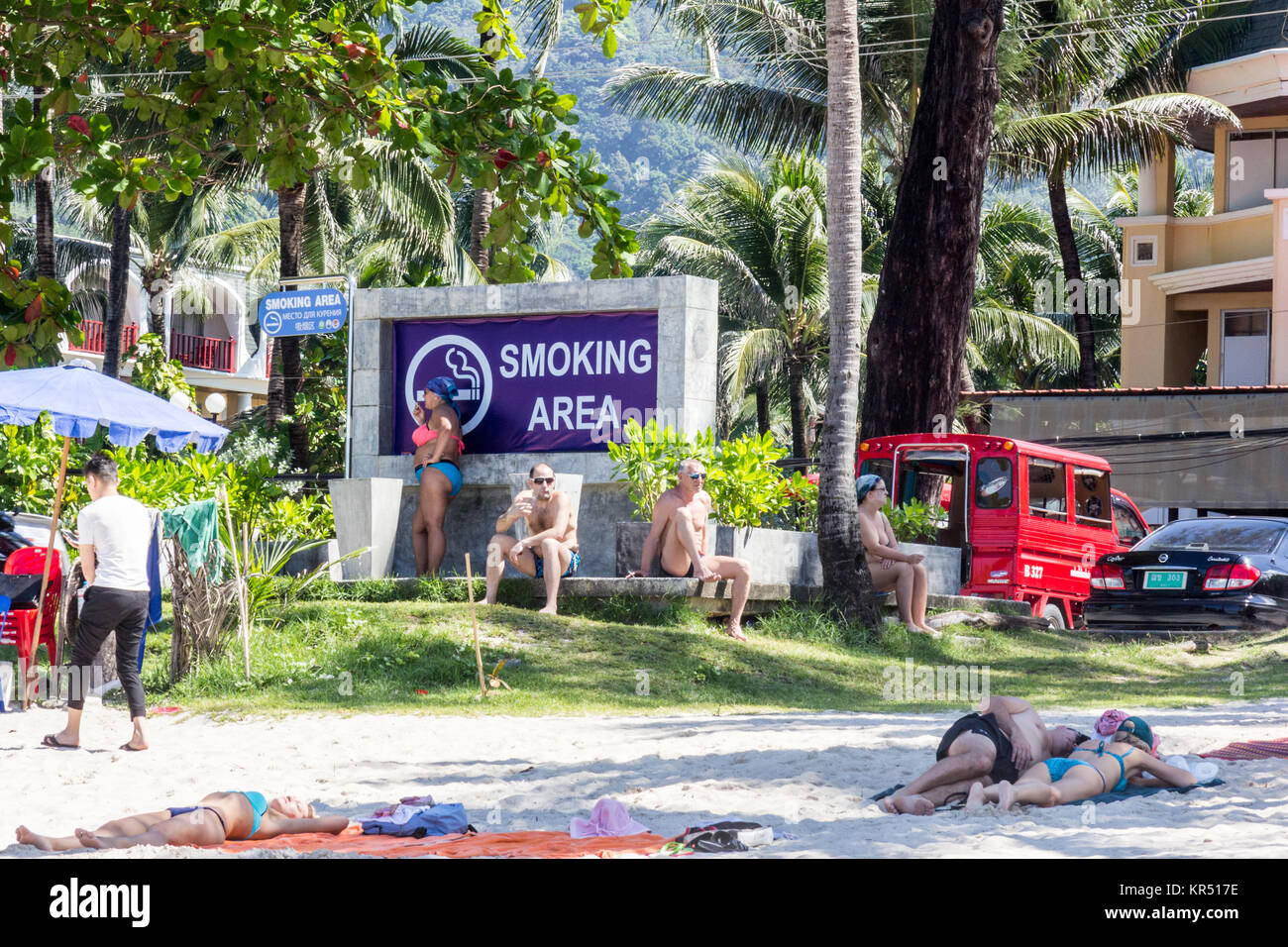 Les touristes de fumer des cigarettes dans une zone fumeurs, Patong Beach, Phuket, Thailand Banque D'Images