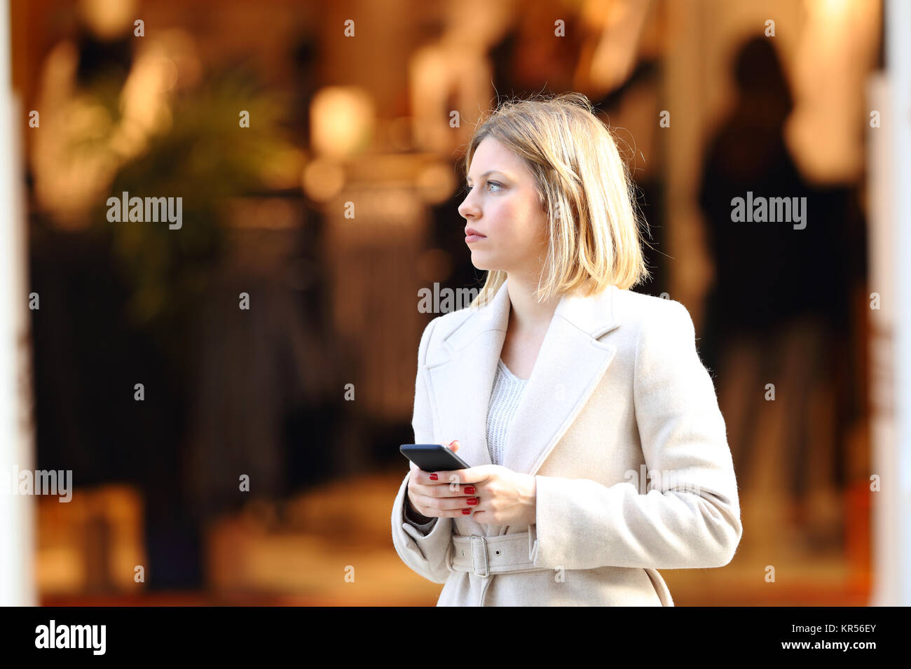 Distrait shopper holding un téléphone intelligent sur la rue avec un magasin à l'arrière-plan en hiver Banque D'Images