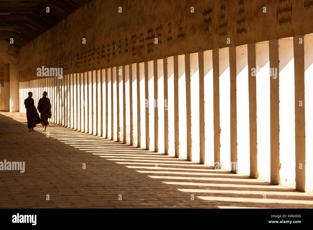 Vue arrière de deux moines à marcher le long de la colonnade ensoleillée de pagode. Banque D'Images