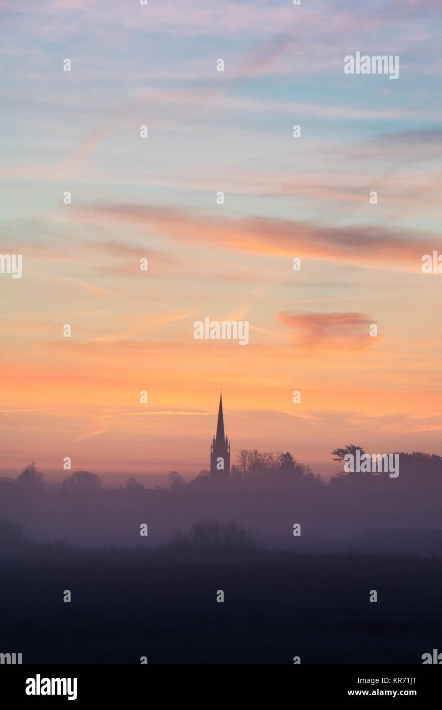 Misty lever du soleil derrière un clocher d'église en décembre. Rois Sutton, Nr Banbury, Northamptonshire, Angleterre Banque D'Images