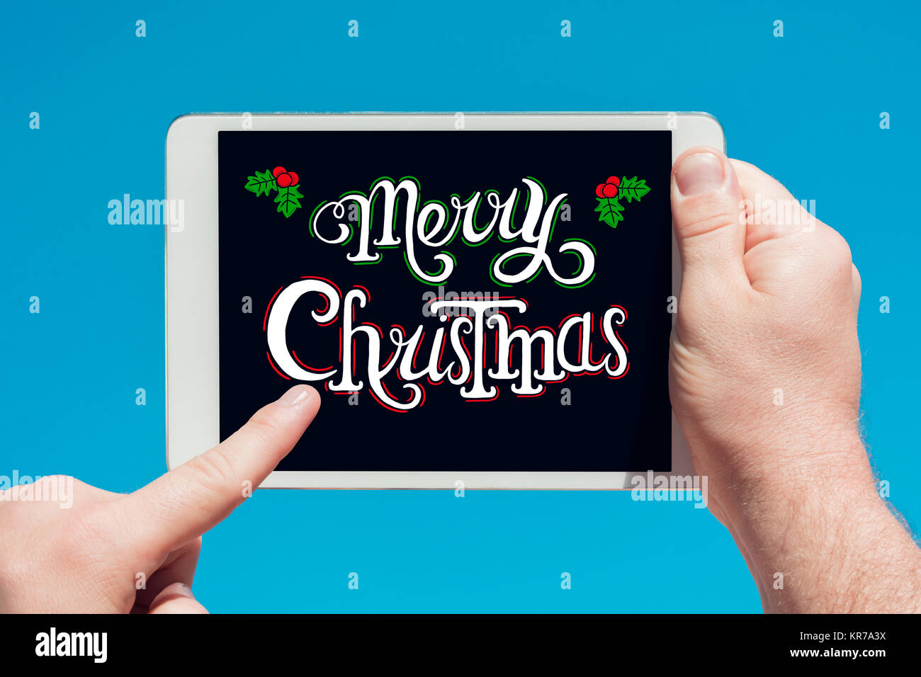 Homme tenant une tablette avec texte 'Merry Christmas' et de toucher l'écran avec un doigt avec ciel bleu en arrière-plan. Banque D'Images