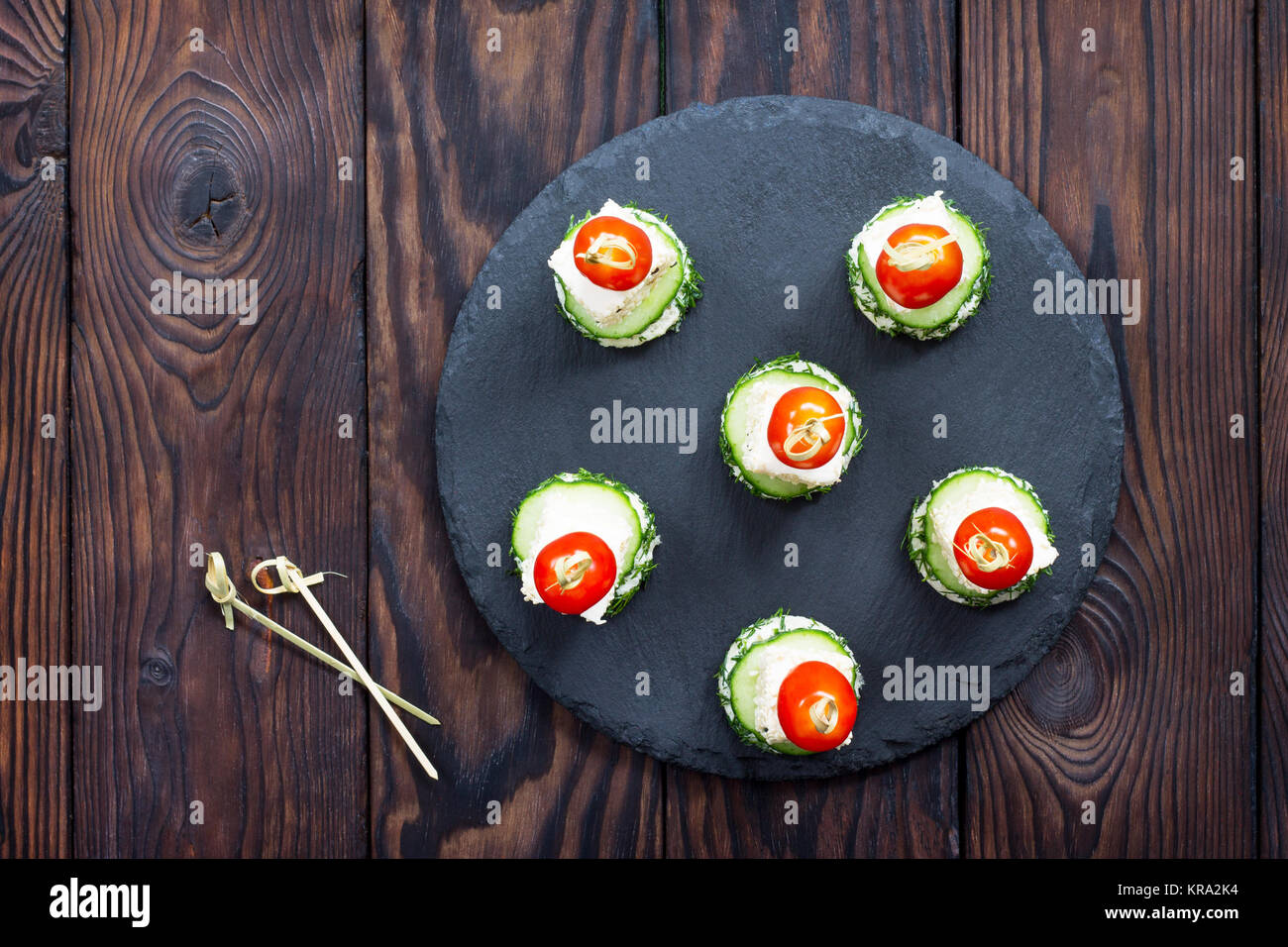 Canape apéritif avec du pain blanc, fromage feta, concombre et tomates cerises sur une table en bois. Banque D'Images