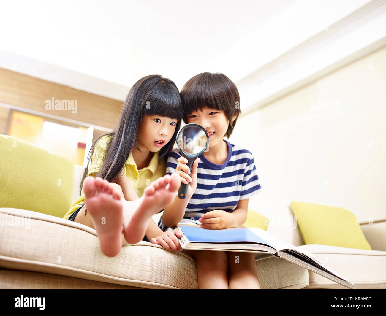 Deux enfants assis sur la table d'Asie à la maison à jouer avec une loupe, low angle view. Banque D'Images