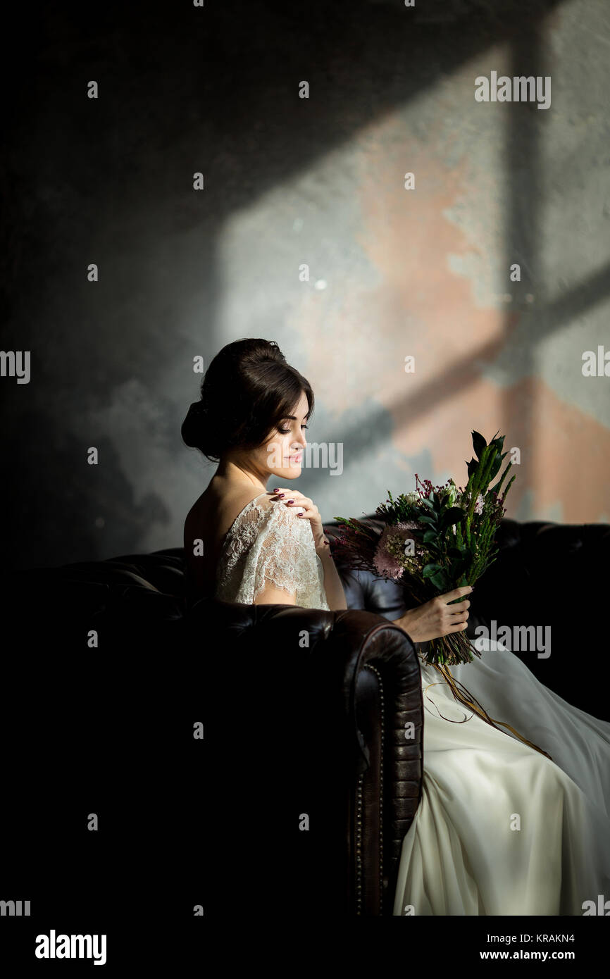 Belle robe de mariée assis sur une chaise à l'intérieur dans dark studio intérieur comme à la maison. Banque D'Images