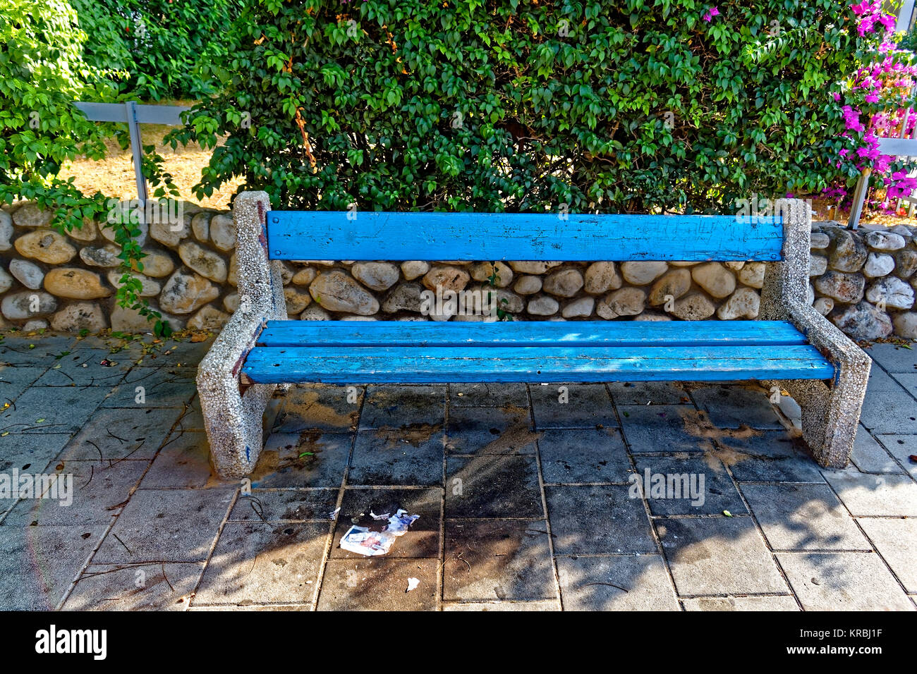 Blue rock et banc en bois sur la rue en face d'un buisson ou d'une clôture Banque D'Images