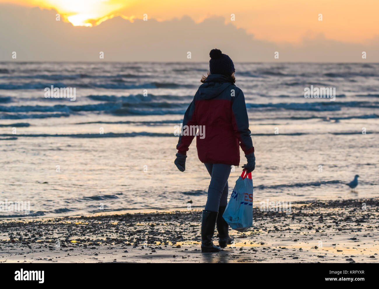Femme marche par le front de mer sur une plage portant un sac de shopping, Tesco en hiver au Royaume-Uni. Banque D'Images