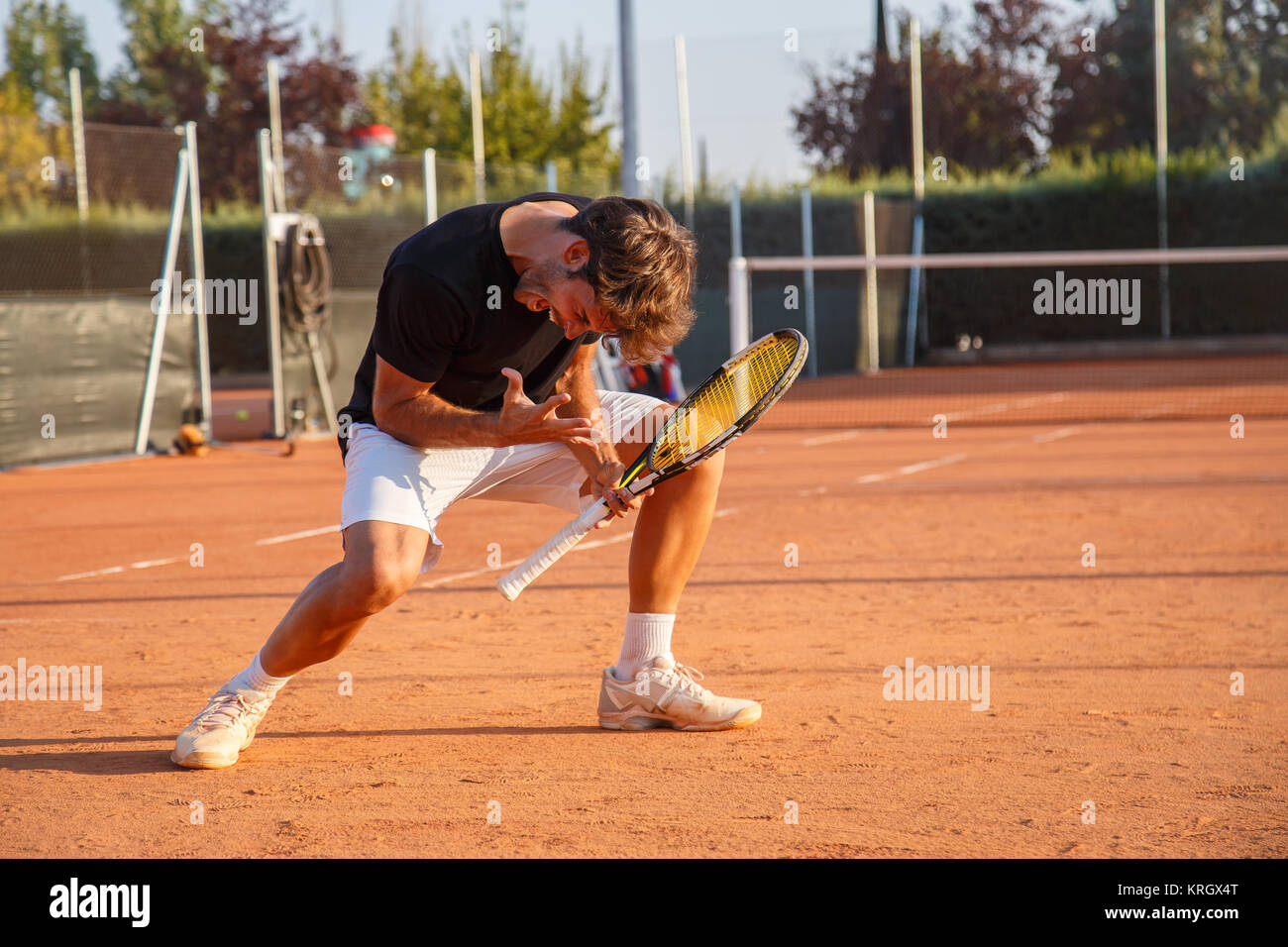 Heureux homme sportif célèbre raquette avec triomphe sur court de tennis en plein soleil à la recherche expressive. Banque D'Images