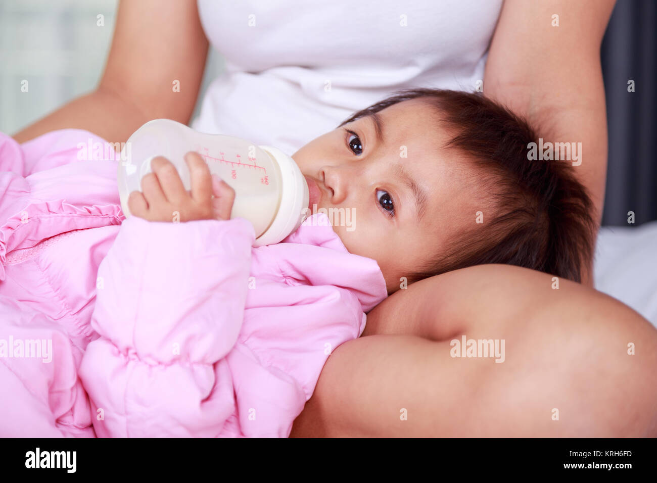 Bébé boit une bouteille de lait avec la mère sur un lit Banque D'Images