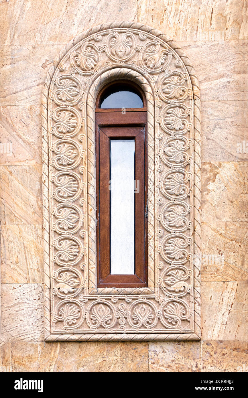 Une belle fenêtre antique avec un châssis allongé étroit et un ornement grec. Mur de lumière brown des dalles en pierre. Banque D'Images