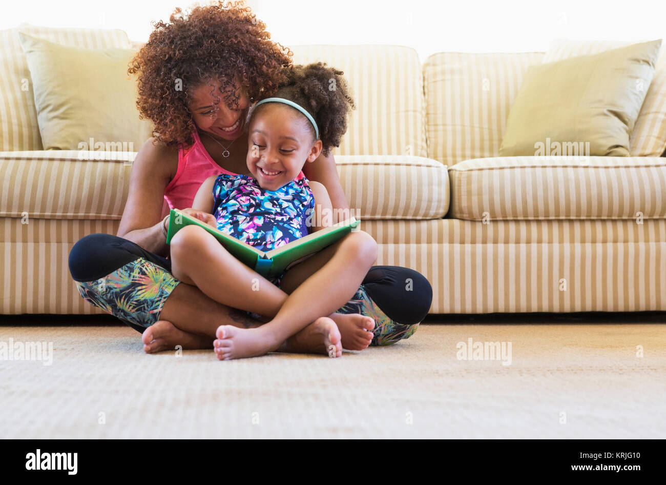 Mixed Race mother and daughter reading book sur le plancher près de canapé Banque D'Images