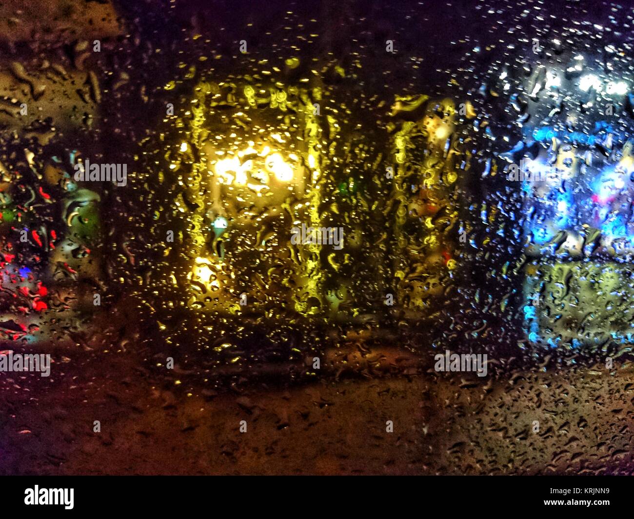 Vitrine lumineuse colorée la nuit vu à travers le verre couverts par des gouttes de pluie. Abstraite de allumé store front sur rue avec porte. Banque D'Images