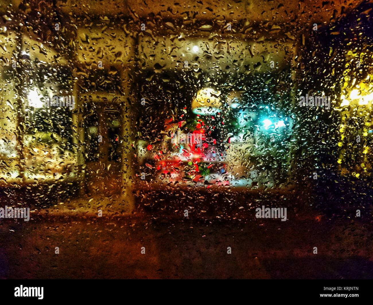 Vitrine lumineuse colorée la nuit vu à travers le verre couverts par des gouttes de pluie. Abstraite de magasin éclairé avec porte avant, entrée privée et desi Banque D'Images