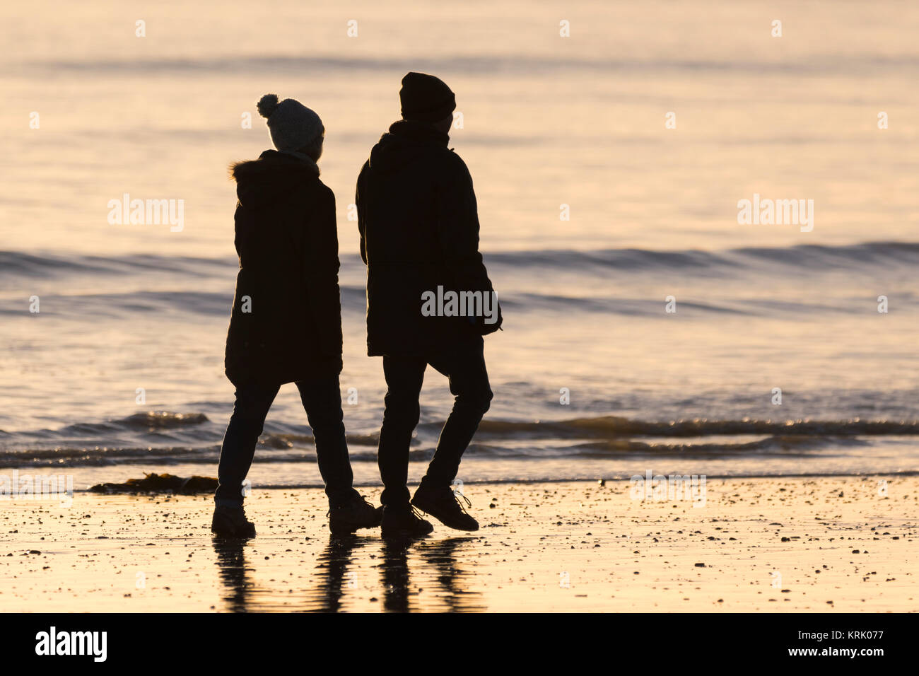 Silhouette d'un couple de prendre une promenade en bord de mer, dans la lumière du soir. Banque D'Images