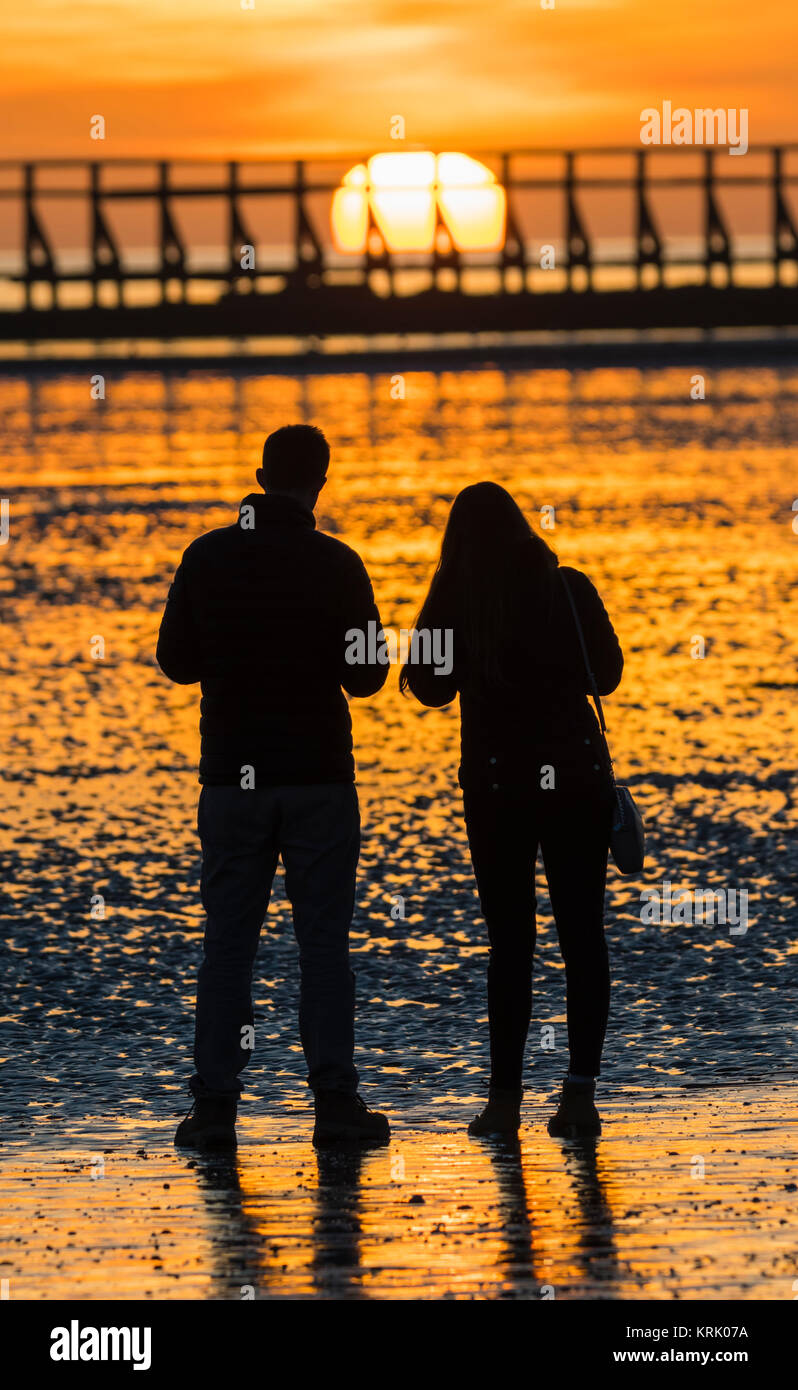 Silhouette d'un couple regardant le coucher du soleil sur une plage en hiver en Angleterre, Royaume-Uni. Portrait. Banque D'Images