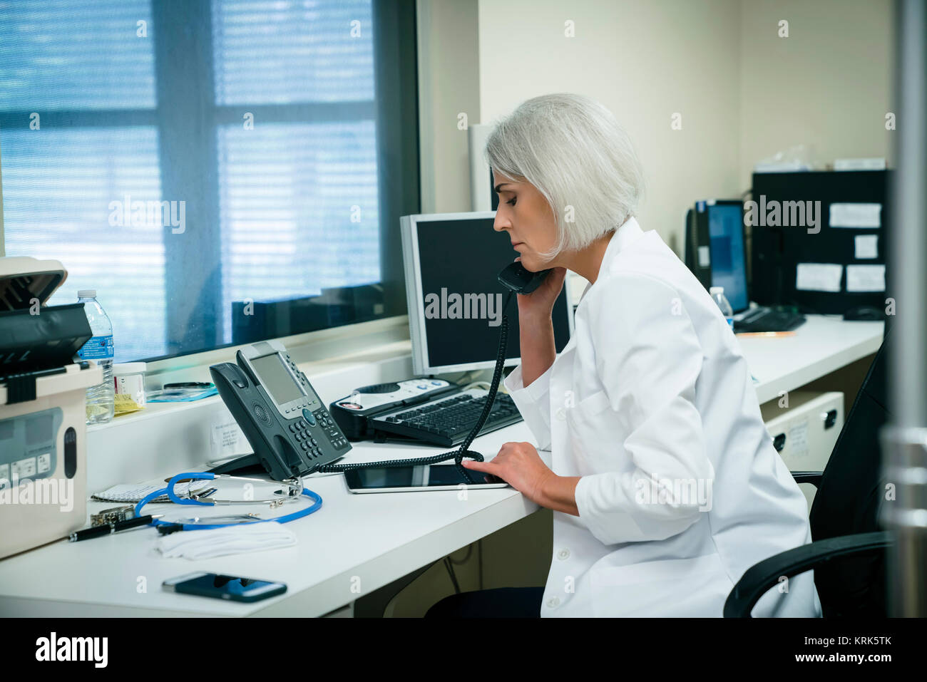 Caucasian doctor talking on telephone et using digital tablet Banque D'Images
