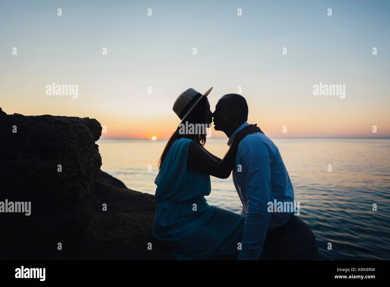 Caucasian couple kissing on rock près de ocean at sunset Banque D'Images