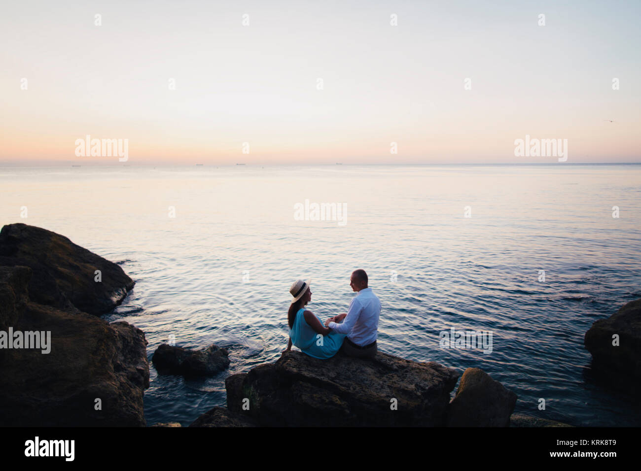 Young couple sitting on rock près de ocean at sunset Banque D'Images
