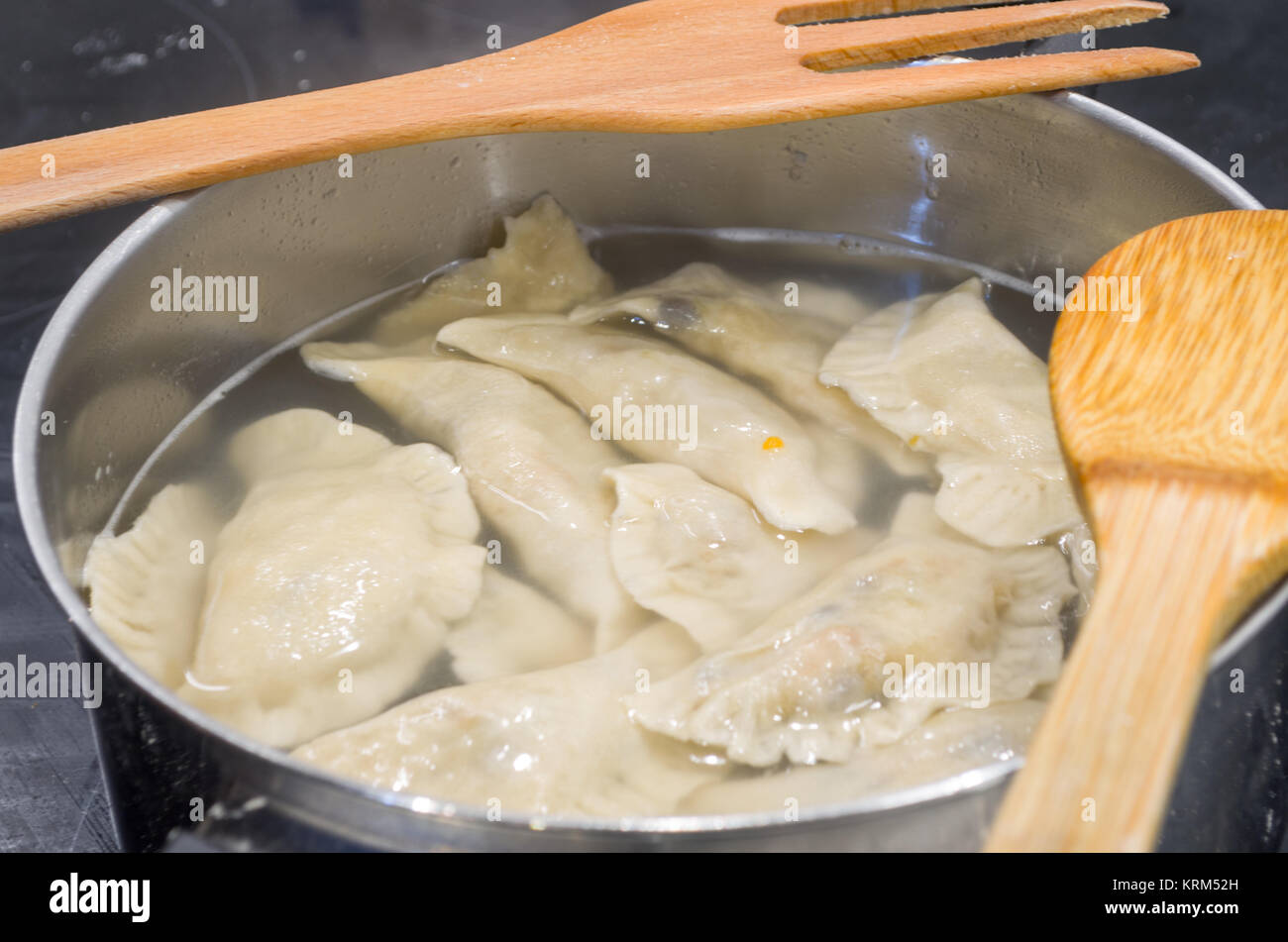 Non-authentique traditionnelle polonaise organisée la veille de Noël dans l'induction de métal moderne pierogies pot rempli d'eau, pendant la préparation- prêt à bouillir. Banque D'Images