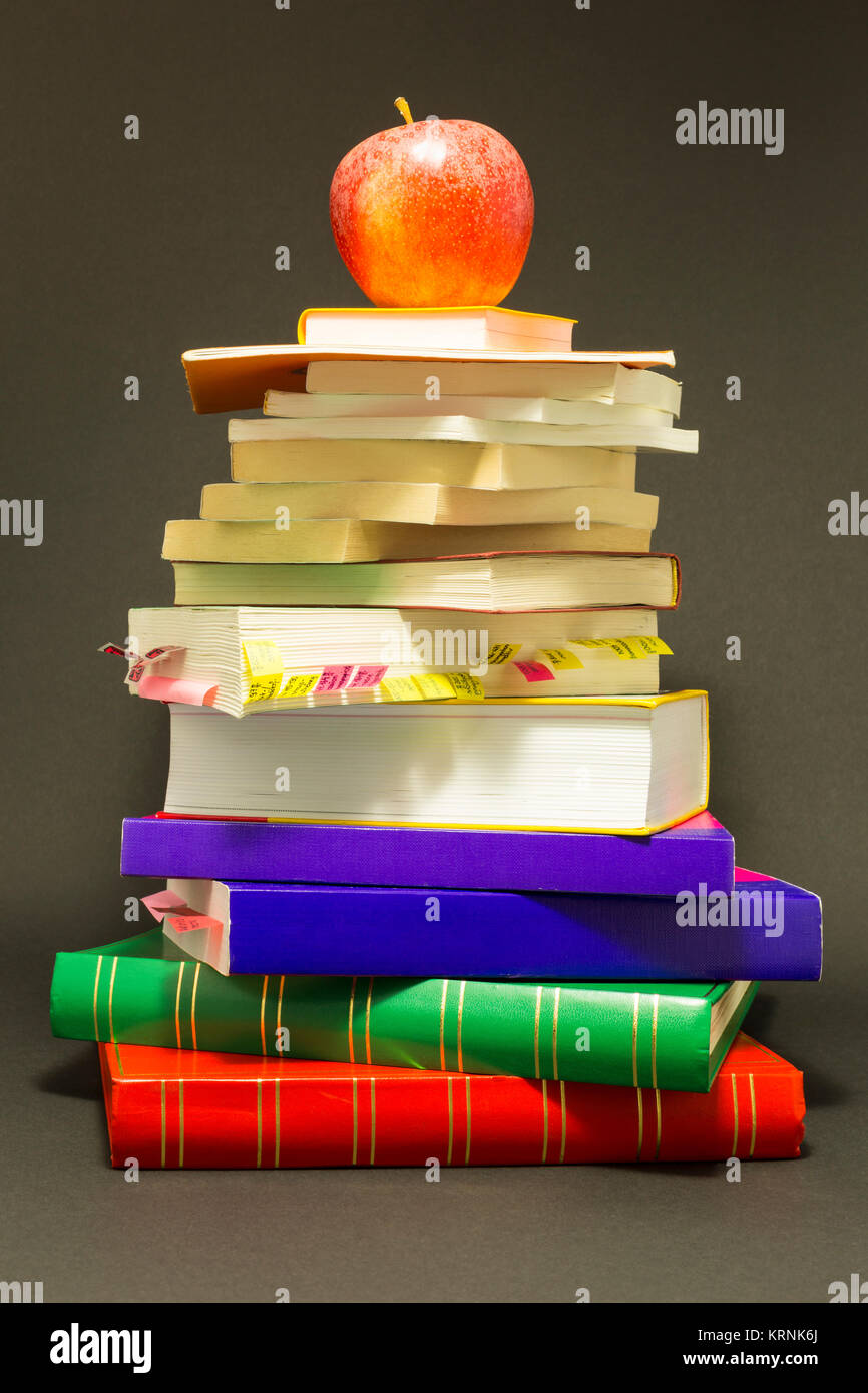 Concept de l'éducation. Pile de livres scolaires avec une pomme rouge en haut en face de fond gris foncé Banque D'Images