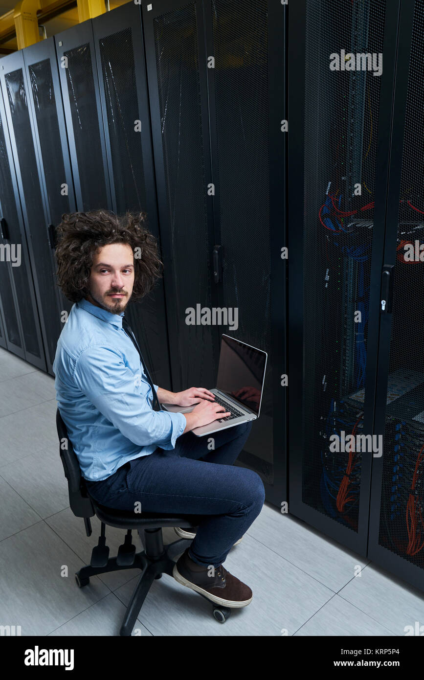 Jeune technicien travaillant sur un ordinateur portable à côté de racks de serveur noir Banque D'Images