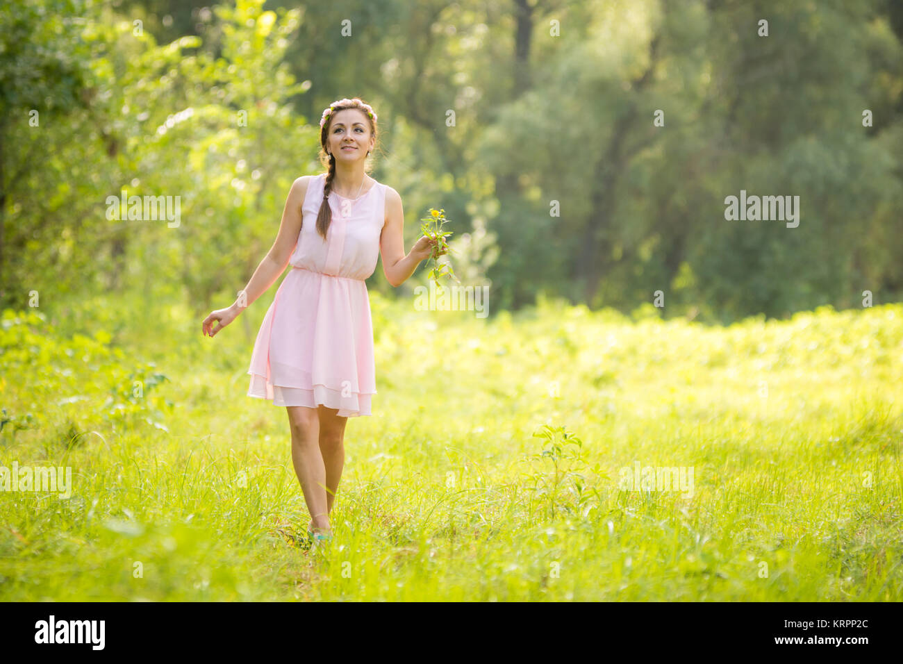 Belle jeune femme marche sur un pré vert avec un bouquet de fleurs sauvages dans une robe d'été légère Banque D'Images