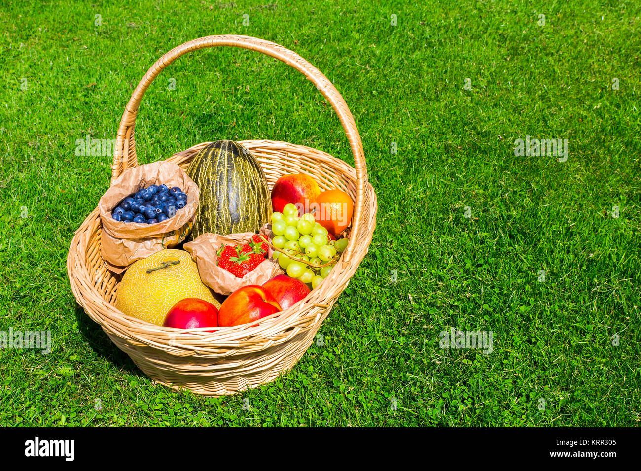 Panier en osier sur l'herbe verte remplie de fruits d'été Banque D'Images