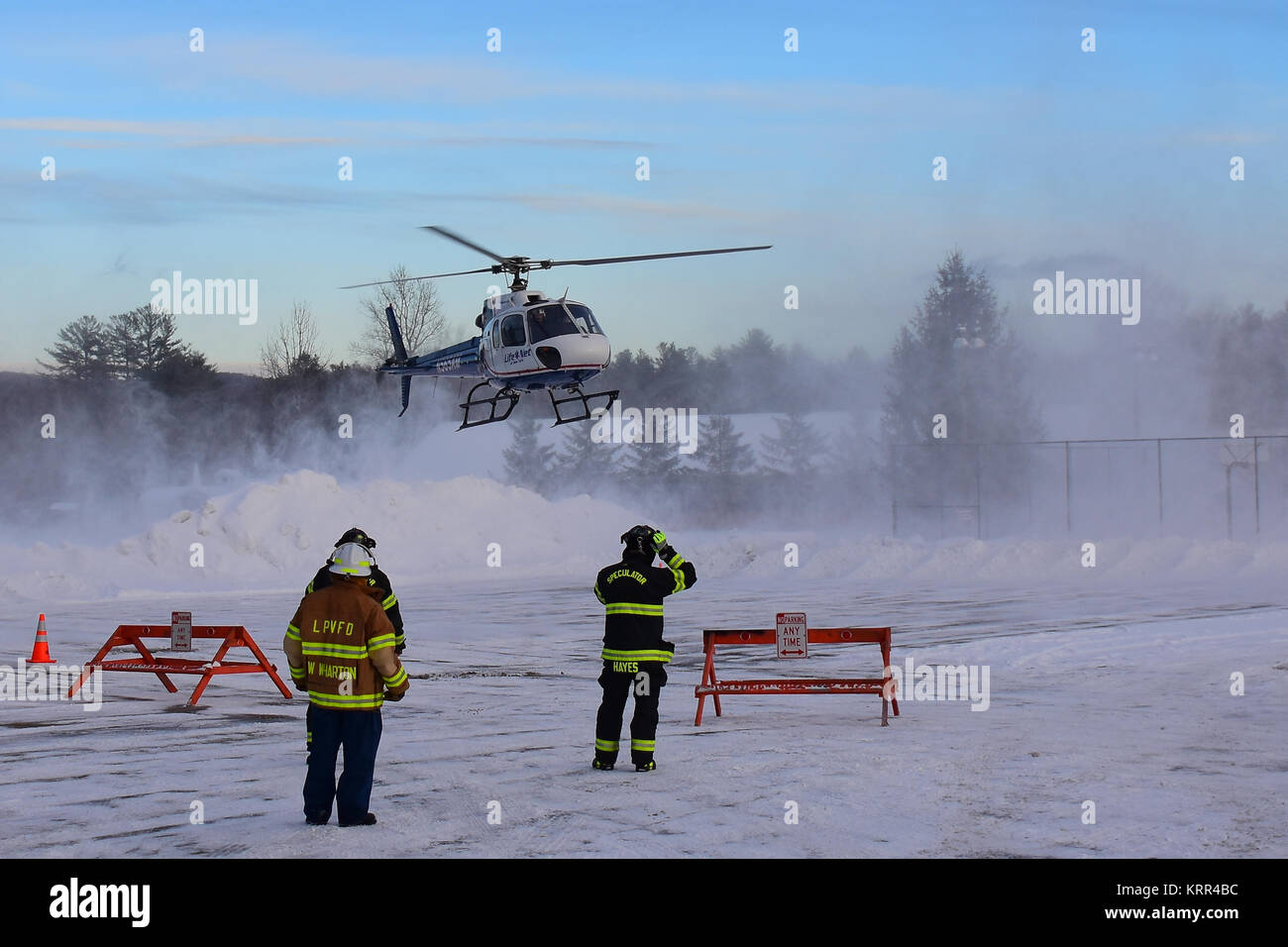 Un hélicoptère d'évacuation d'urgence qui viennent pour un atterrissage sur une hélisurface couvertes de neige avec deux pompiers prêt à assister. En spéculateur, NY, USA Banque D'Images