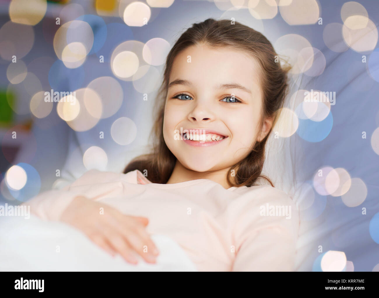 Happy smiling girl lying awake au lit plus de lumières Banque D'Images
